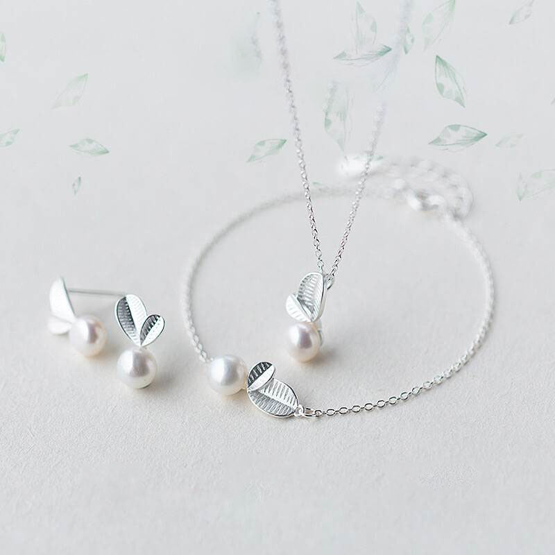 A necklace wit a leaf ana a peral suspended on the center within a bracelet and earring studs of the same design