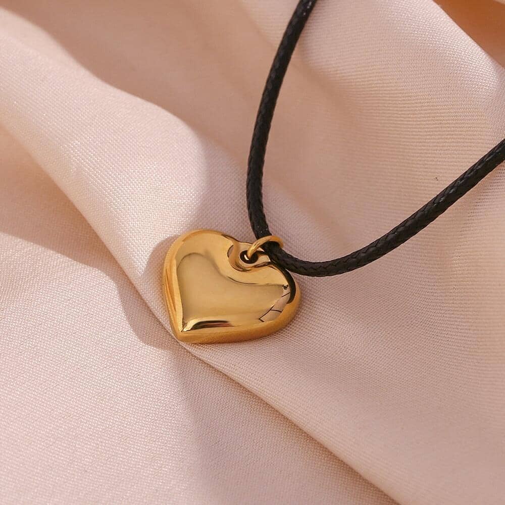 a rope necklace with a gold heart pendant on a textil surface
