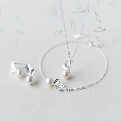 A necklace wit a leaf ana a peral suspended on the center within a bracelet and earring studs of the same design